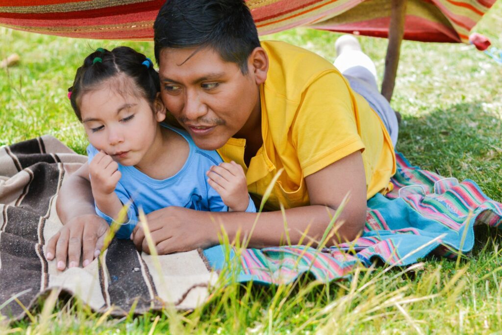Latin dad with his little daughter having good time in the hovel made from clothing in the countryside.